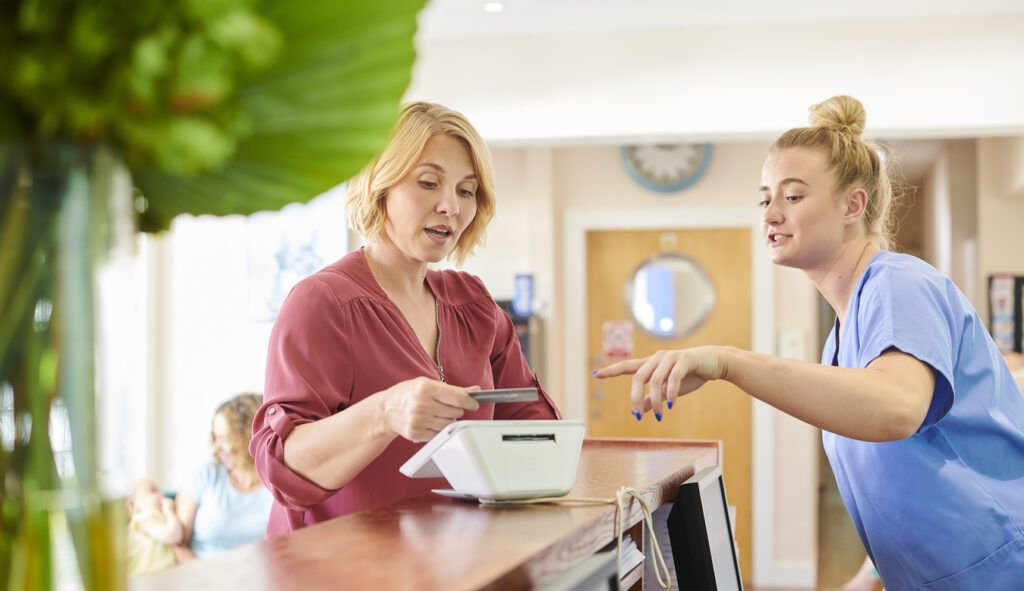 female patient chats to the nurse whilst paying at reception of medical practice
