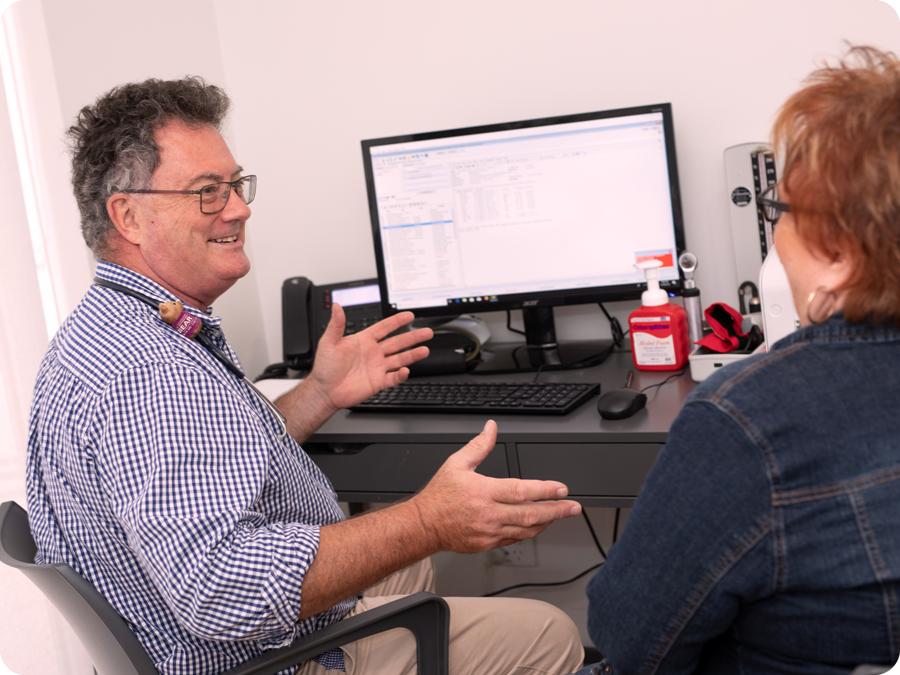 Doctor sitting in medical practice with patient on computer with genie software on screen